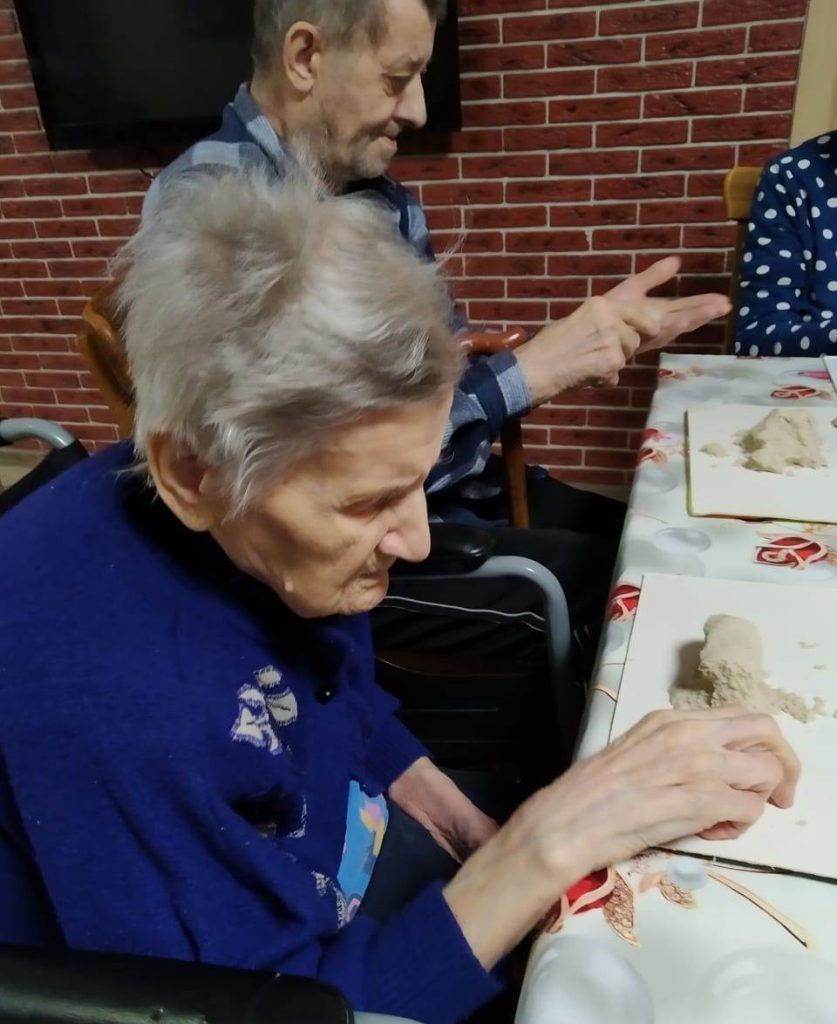 Пожилые постояльцы дома престарелых готовят пирожки из песка для лепки